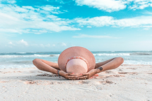 kvinne med hatt ligger på stranden